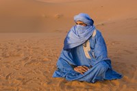 Veiled Tuareg man sitting cross-legged on the sand, Erg Chebbi, Morocco Fine Art Print